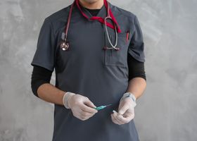 Healthcare worker with stethoscope holding a syringe ready for injection.